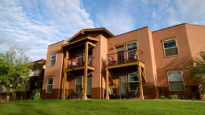 Back of house with a patio area, a balcony, stucco siding, and a lawn