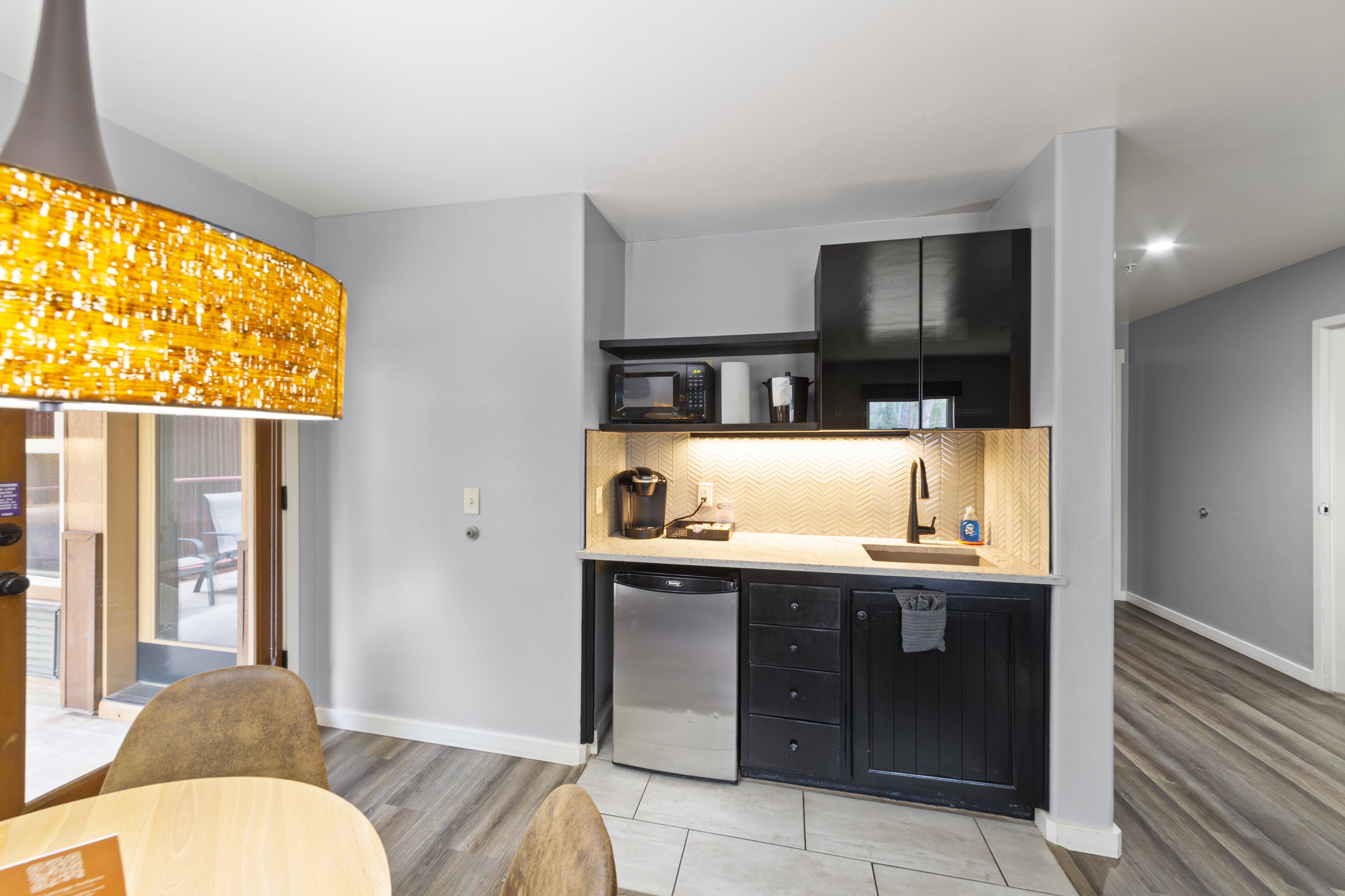 Bar featuring dark cabinets, stainless steel refrigerator, light wood-style floors, black microwave, and light stone counters