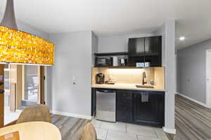 Bar featuring dark cabinets, stainless steel refrigerator, light wood-style floors, black microwave, and light stone counters