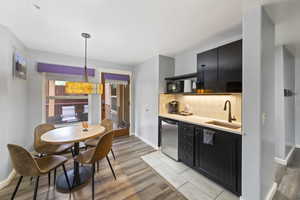 Kitchen with dark cabinets, light wood finished floors, backsplash, and dishwasher