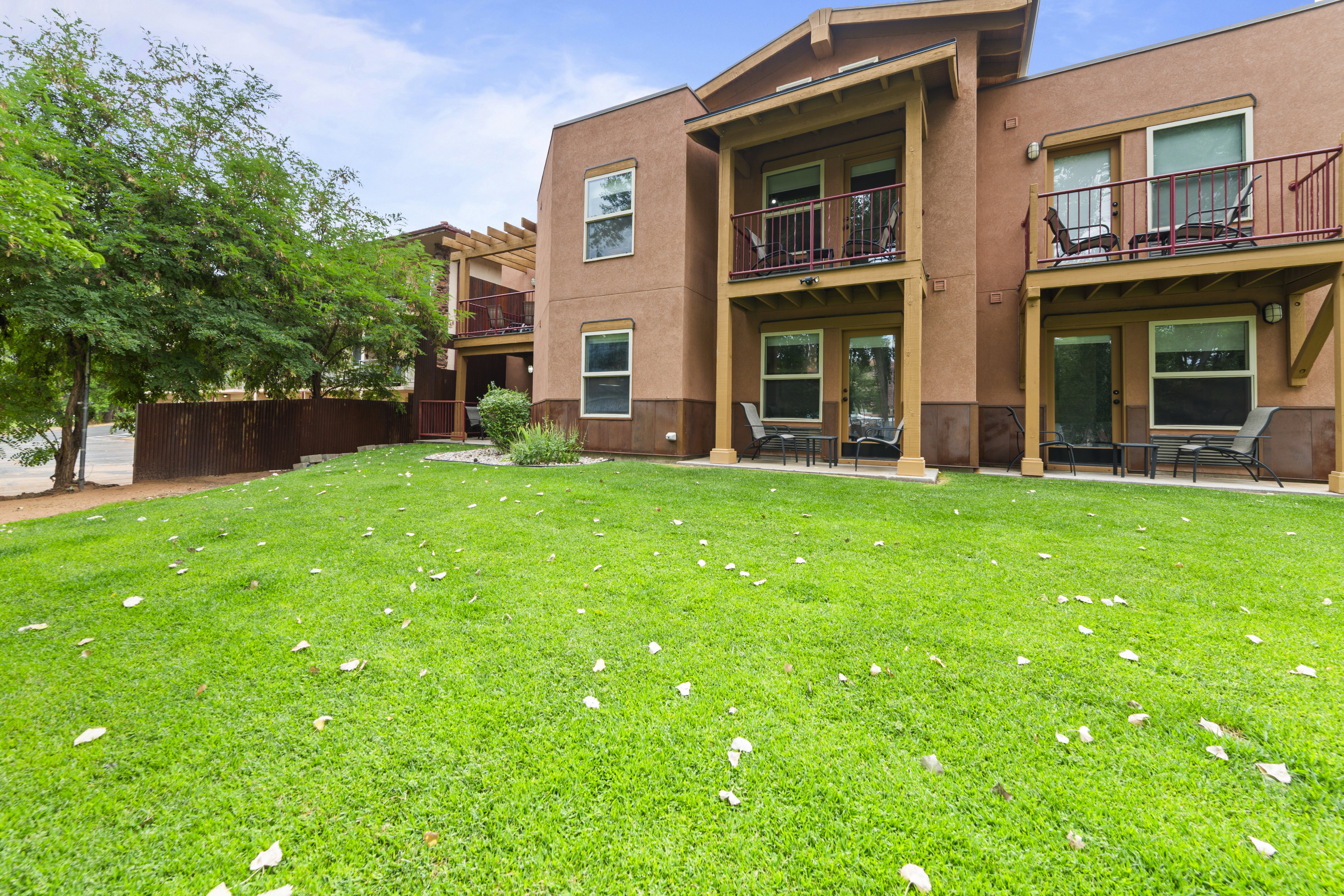 Back of house with a patio area, stucco siding, a balcony, and a lawn
