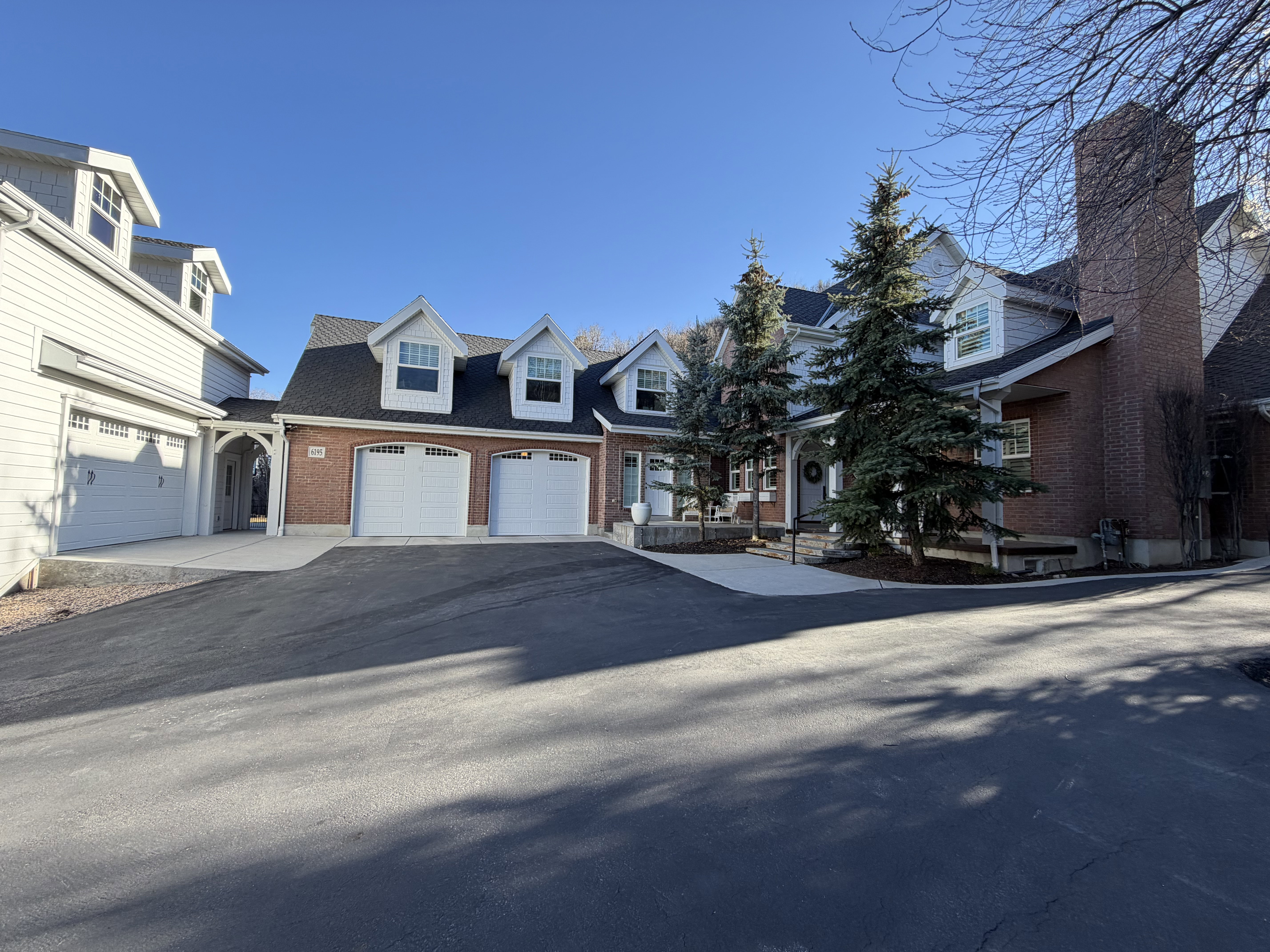 Brick and siding exterior featuring multiple dormer windows, a prominent brick chimney, and mature evergreen trees