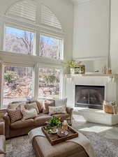 Living area featuring a brick fireplace, a high ceiling, plenty of natural light, and ornamental molding