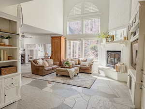 Living room featuring a brick fireplace, a ceiling fan, a high ceiling, and stone floors