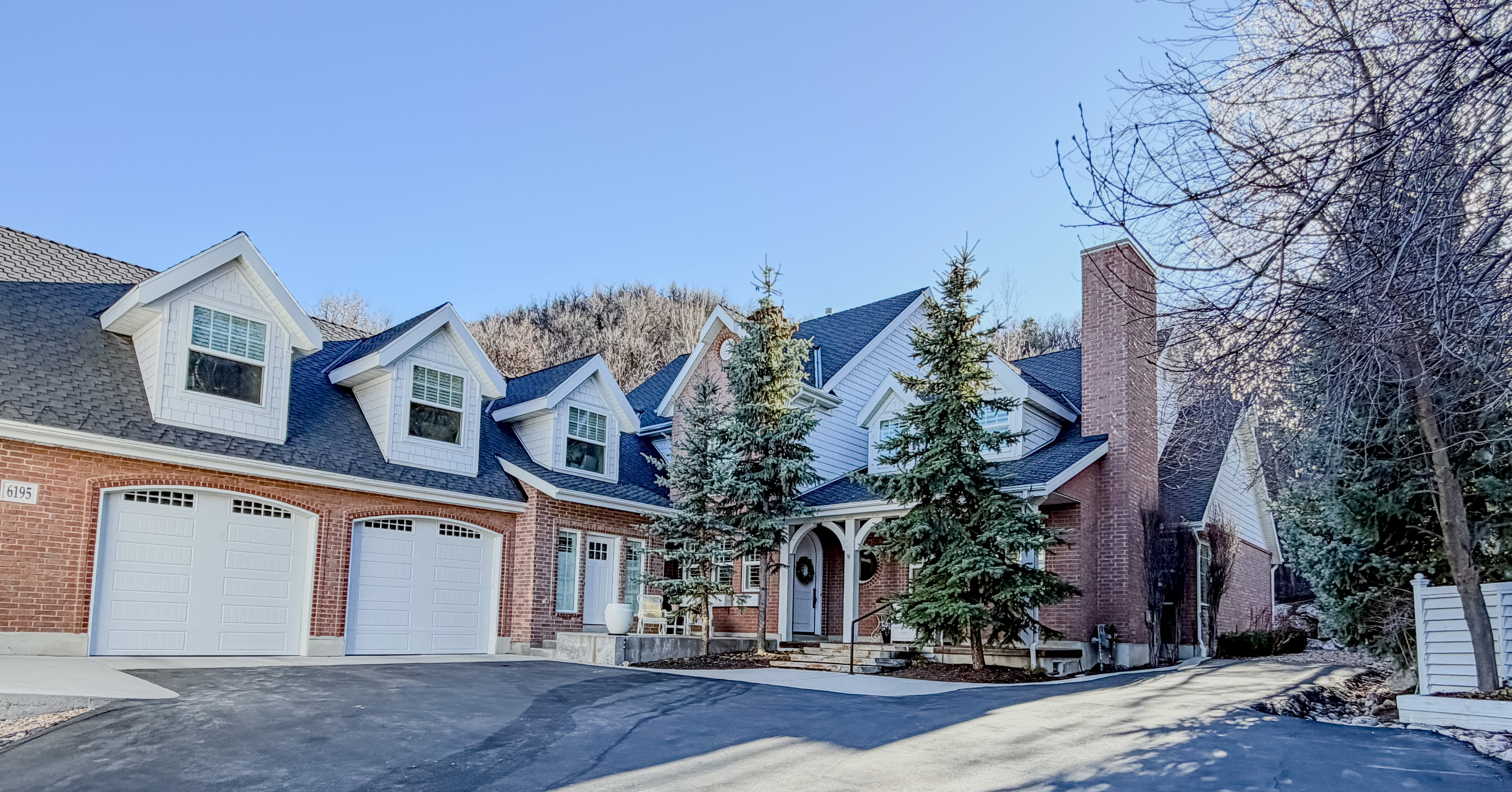 Cape cod home featuring asphalt driveway, a shingled roof, brick siding, and an attached garage