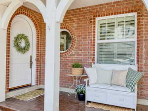 View of exterior entry featuring brick siding and covered porch