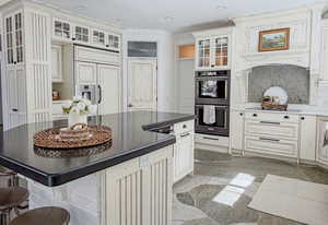 Kitchen with a center island, glass fronted cabinets, multiple ovens, a kitchen breakfast bar, and recessed lighting