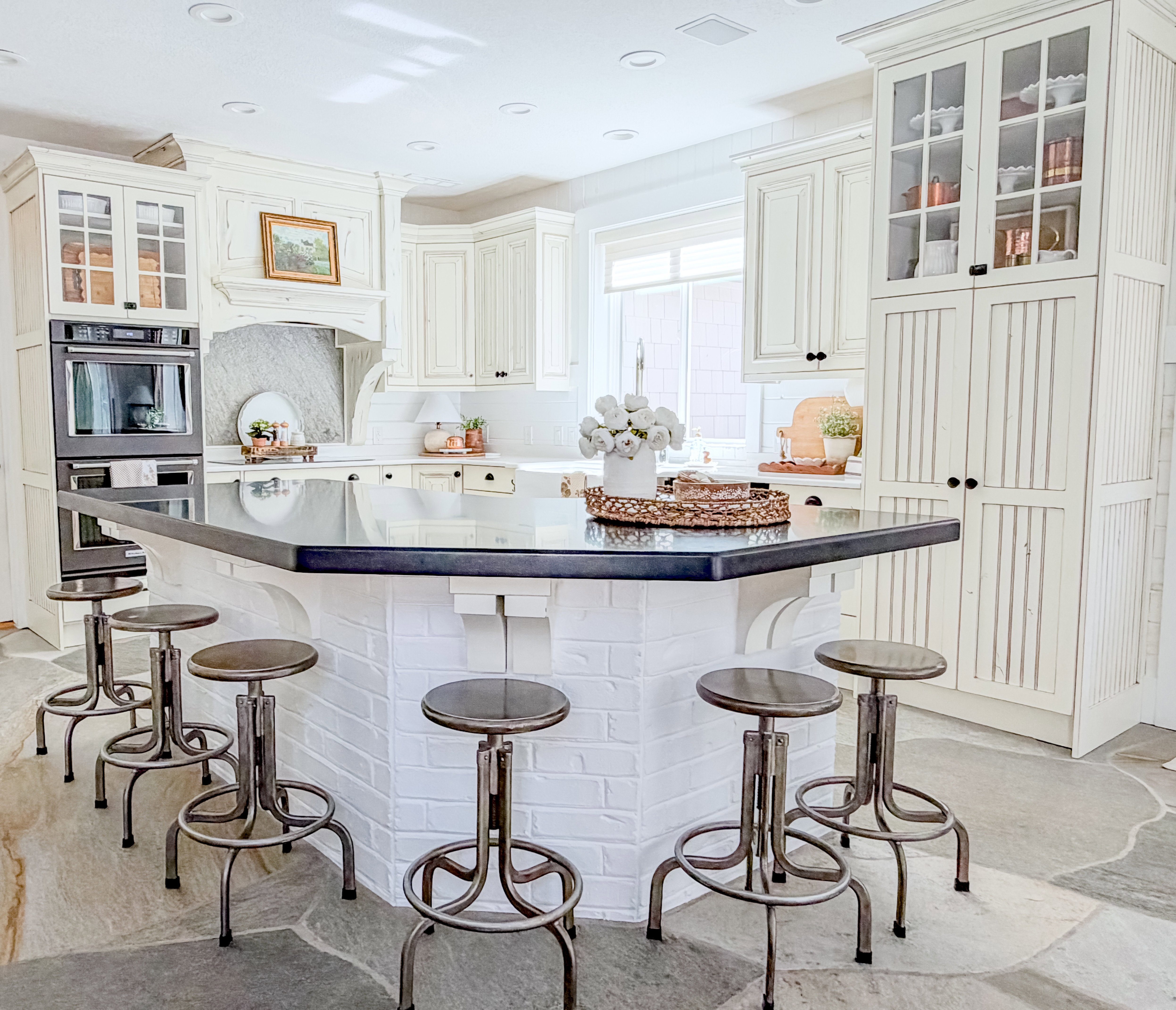 Kitchen featuring glass insert cabinets, light stone finish floors, stainless steel double oven, a breakfast bar, and a center island