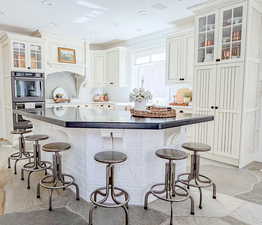 Kitchen featuring glass insert cabinets, light stone finish floors, stainless steel double oven, a breakfast bar, and a center island