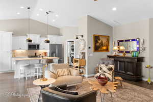 Living room with dark wood finished floors, lofted ceiling, stacked washer / drying machine, recessed lighting, and ceiling fan