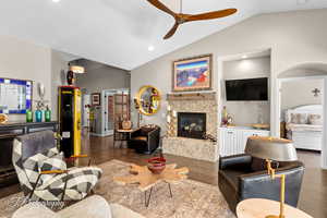 Living room featuring vaulted ceiling, wood finished floors, a tiled fireplace, recessed lighting, and ceiling fan