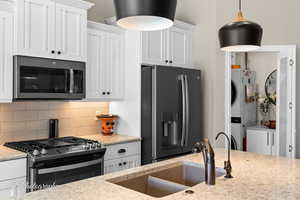 Kitchen with backsplash, white cabinets, stainless steel appliances, stacked washer and clothes dryer, and light stone countertops
