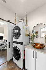 Laundry area featuring dark wood-style floors, stacked washer / dryer, and a desk