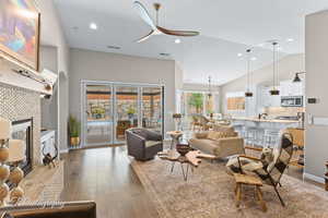 Living room featuring ceiling fan, a fireplace, dark wood-style floors, hanging lights, and lofted ceiling