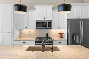 Kitchen featuring tasteful backsplash, white cabinets, stainless steel appliances, and light stone counters