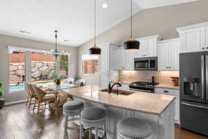 Kitchen with white cabinets, stainless steel appliances, a breakfast bar, decorative backsplash, and lofted ceiling