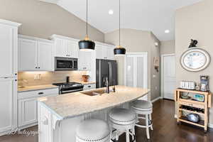 Kitchen with white cabinets, an island with sink, stainless steel appliances, a kitchen bar, and vaulted ceiling