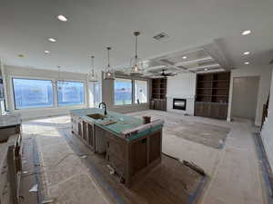 Kitchen featuring ceiling fan, a glass covered fireplace, an island with sink, open floor plan, and coffered ceiling