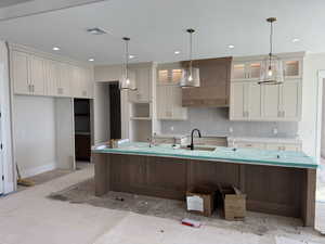 Two tone kitchen featuring an island with sink, two tone cabinetry, pendant lighting, glass fronted cabinets, and light countertops