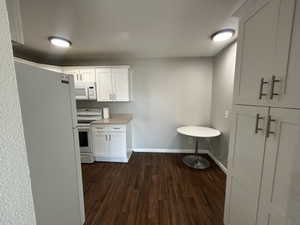 Kitchen featuring white appliances, white cabinetry, light countertops, and dark wood-style flooring