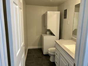 Bathroom featuring a textured wall, vanity, stacked washer and clothes dryer, electric panel, and dark tile patterned flooring