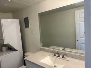 Bathroom featuring a textured wall, vanity, stacked washing machine and dryer, electric panel, and a textured ceiling