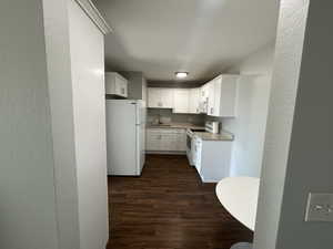 Kitchen featuring a textured wall, white appliances, dark wood-style floors, white cabinets, and light countertops