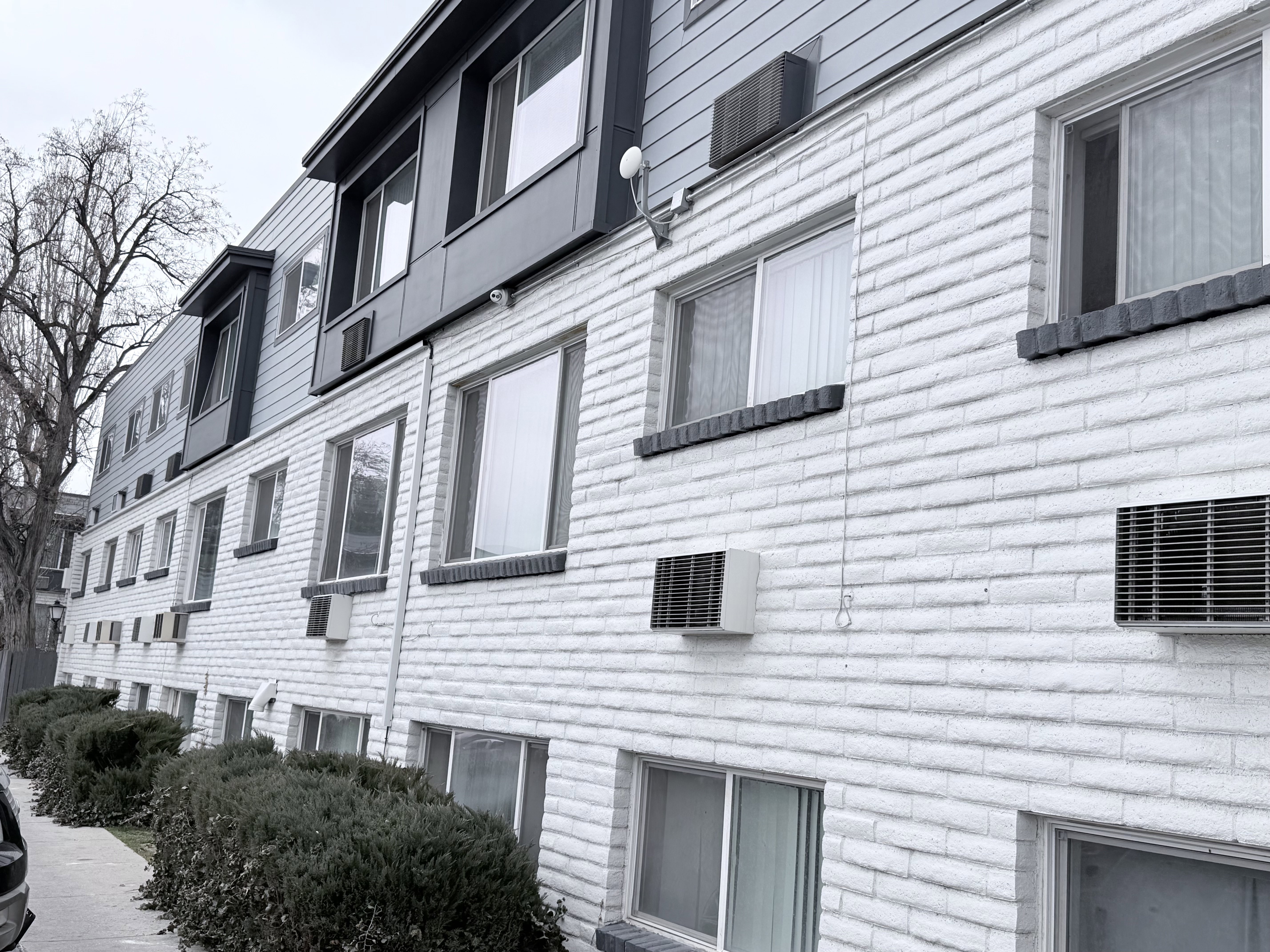 Multi-story building featuring white painted brick on the lower levels and horizontal siding on the upper floors