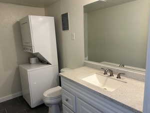 Bathroom with a textured wall, vanity, dark tile patterned floors, stacked washer and dryer, and electric panel