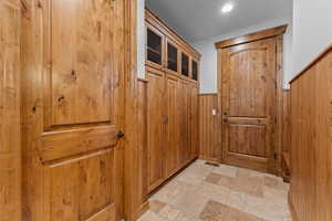 Doorway to outside featuring stone tile flooring, wooden walls, wainscoting, and recessed lighting