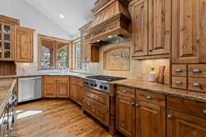 Kitchen with lofted ceiling, light wood finished floors, wood finish cabinetry, stainless steel appliances, and tasteful backsplash