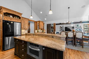 Kitchen featuring stainless steel appliances, vaulted ceiling, glass fronted cabinets, light stone counters, and a center island