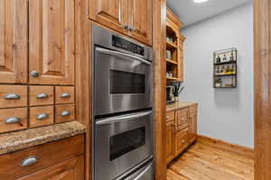 Kitchen with double oven, light wood-style flooring, wood finish cabinetry, and light stone counters