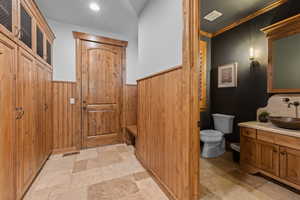 Half bath with vanity, light stone finish flooring, wooden walls, and crown molding