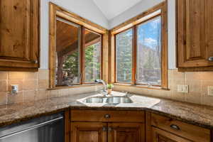 Kitchen featuring backsplash, wood finish cabinets, dark stone counters, stainless steel dishwasher, and lofted ceiling