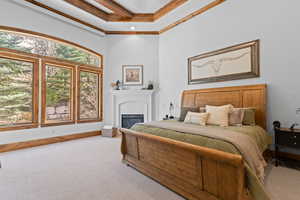 Carpeted bedroom featuring crown molding, a glass covered fireplace, and a high ceiling