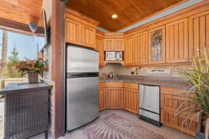 Kitchen featuring stainless steel appliances, glass insert cabinets, wood ceiling, wood finish cabinets, and dark countertops