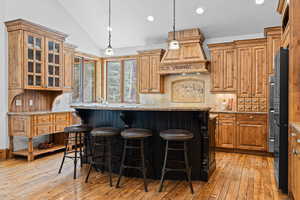 Kitchen with vaulted ceiling, light stone countertops, light wood-type flooring, decorative light fixtures, and a breakfast bar
