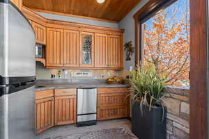 Kitchen with stainless steel appliances, wood ceiling, wood finish cabinetry, glass insert cabinets, and dark countertops