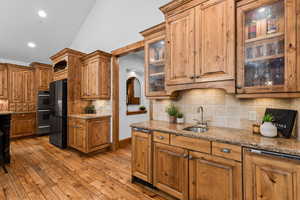 Kitchen featuring glass insert cabinets, light stone countertops, lofted ceiling, decorative backsplash, and light wood-type flooring