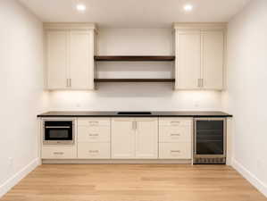 Kitchenette featuring light-toned cabinetry, dark countertops, and wood-finish flooring. Microwave and beverage fridge.