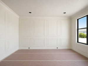 Room featuring full wall paneling with decorative molding, crown molding, a large black-framed window, and recessed ceiling lighting