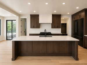 Spacious kitchen island with a light-toned countertop, dark wood-finish cabinetry, black appliance suite, recessed lighting, and wood-finish flooring.