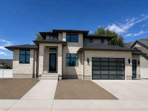 Modern exterior featuring a stone and stucco facade, a dark shingled roof, a contemporary front entry, and 3-car garage.  South facing home.