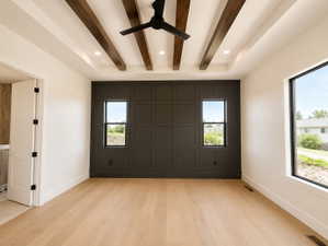 Spacious primary bedroom featuring a tray ceiling with stained wood beams, a black ceiling fan, and recessed lighting