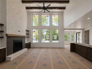 Two-story living area featuring a stone fireplace with a wood mantle, custom built-in shelving, soaring ceilings with exposed wood beams, and a large multi-pane window configuration