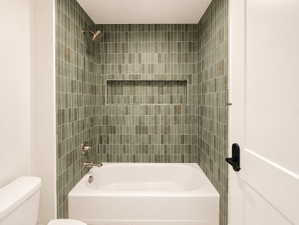 White bathtub and shower combination featuring green rectangular tile, a built-in shower niche, and brushed nickel fixtures.  Separate area from sink.