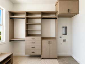 Custom closet system featuring light wood-finish cabinetry, built-in shelving, and drawers with matte black hardware Washer and dryer hook-ups.