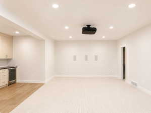 Spacious entertainment area featuring recessed lighting, a ceiling-mounted projector, and integrated wall speaker cutout.  Next to kitchenette
