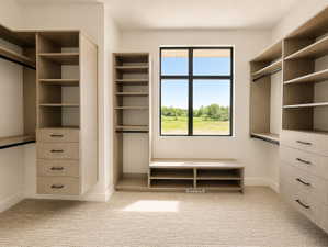 Custom closet system featuring light wood-finish cabinetry, built-in shelving, drawers with matte black hardware, and an integrated storage bench.  Exterior window on front of home.